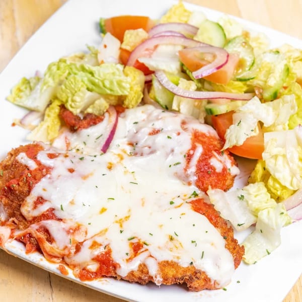 Chicken Parmesan with melted mozzarella, marinara sauce, and a side salad with lettuce, tomatoes, and red onions.