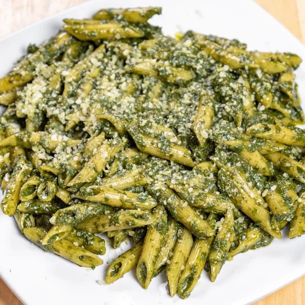 Penne pasta with vibrant green pesto sauce and grated cheese on a white plate.