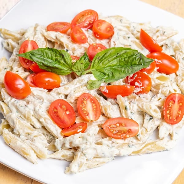 Penne pasta in a creamy sauce, topped with halved cherry tomatoes and fresh basil leaves.