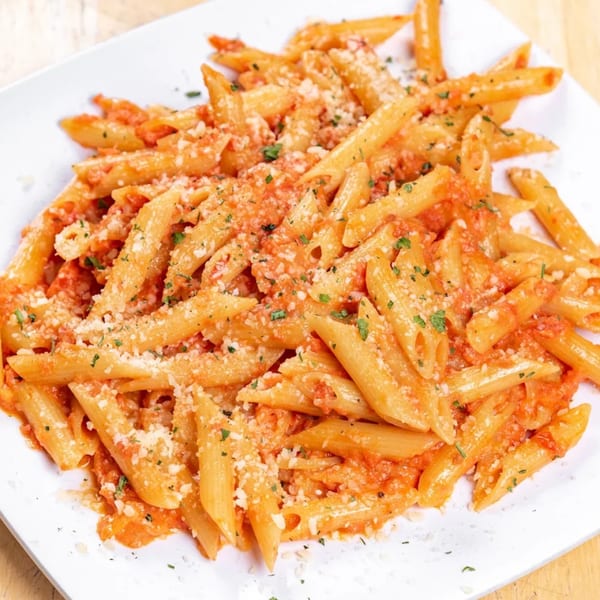 Penne pasta with red sauce, grated cheese, and parsley on a white rectangular plate.