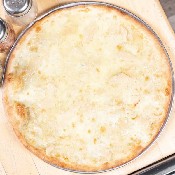 A whole white pizza with a golden crust, topped with cheese and garlic, on a wooden surface.